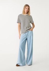 Stribet bomulds t-shirt i creme og navy, parret med lyseblå wide-leg jeans. Lange ærmer, rund halsudskæring og snoretræk i taljen.