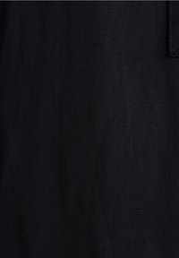 Nahaufnahme von schwarzem strukturiertem Stoff mit diagonaler Webstruktur, die einen Teil einer Naht und eine genähte Kante zeigt.