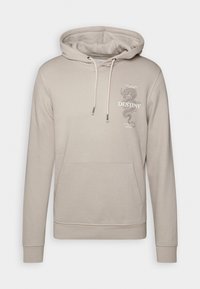 Sudadera con capucha beige hecha de un tejido suave, con un bolsillo frontal, capucha con cordón y una impresión gráfica de un dragón con la palabra "DESTINO".