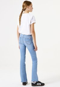 Weißes T-Shirt mit kurzen Ärmeln, hellblaue Schlagjeans, schwarze Sneaker mit weißen Streifen. Einfaches Design, glatte Textur und lässige Passform.