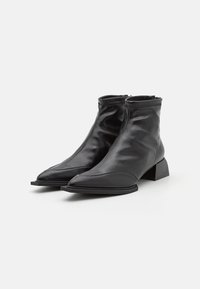 Bottes basses en cuir noir avec un bout pointu et un petit talon carré. Elles présentent un design sans coutures avec des détails texturés à la cheville.