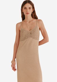 Pletené midi šaty v béžové barvě s krajkovým detailem na korzetu, tenkými ramínky a žebrovanou strukturou od pasu dolů. Elegantní a přiléhavý silueta.