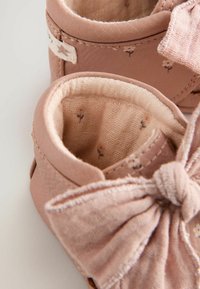Weiche, rosa Lederstiefel mit strukturiertem Finish, ausgestattet mit einer Stoffschleife und einem floralen Innenfutter. Die abgerundete Form verbessert die Passform.