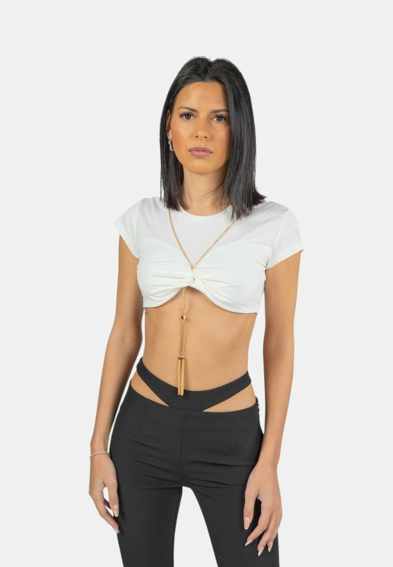 Top bianco corto con design frontale attorcigliato, abbinato a pantaloni neri a vita alta con dettagli a taglio e una collana in oro.