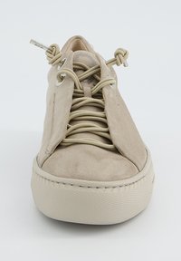 Bēšas zamšādas kedas ar teksturētu gumijas zoli, kurām ir mezgloti šņorējumi un metāla acs elementi, kas piedod unikālu dizaina akcentu.