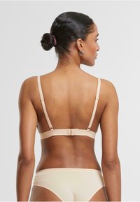 Nude-colored bra with adjustable straps and a hook-and-eye closure at the back, featuring a smooth texture and minimalistic design.