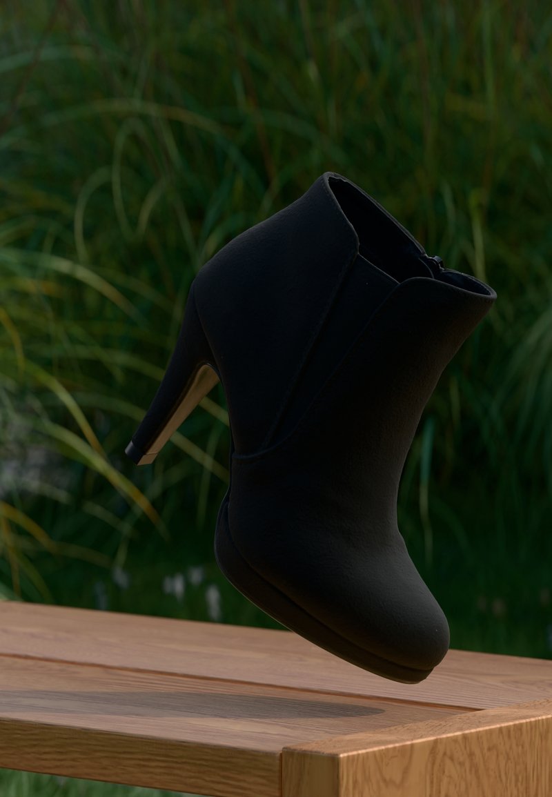 Bottine noire à talon haut suspendue au-dessus d'une table en bois avec des plantes vertes floues en arrière-plan.