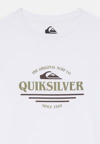 Biela bavlnená tričko s centrálnou grafikou v olivovo zelenej a tmavo hnedej farbe, s nápisom "QUIKSILVER" a "THE ORIGINAL SURF CO SINCE 1969."