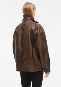 Pruun nahast jope, millel on kõrge kaelus, elastne lõpp ja vabalt lõigatud siluett koos nähtavate õmblustdetailidega. Sujuv tekstuur.