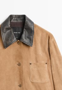 Giacca in camoscio color beige con colletto in pelle nera. Presenta una tasca anteriore, bottoni in metallo e una texture liscia. Etichetta: Massimo Dutti.