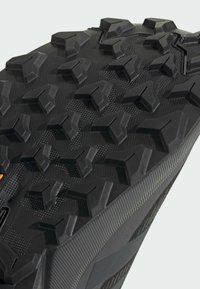Primo piano di una suola in gomma nera con profondi motivi di battistrada multidirezionali progettati per una forte aderenza e trazione all'aperto.