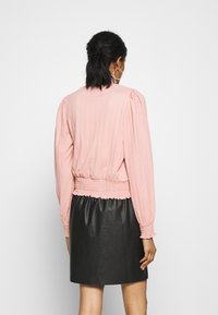 Blusa rosa con texture, maniche a sbuffo e orlo arricciato, abbinata a una gonna di pelle nera. Design semplice; nessun motivo o accessorio notevole.