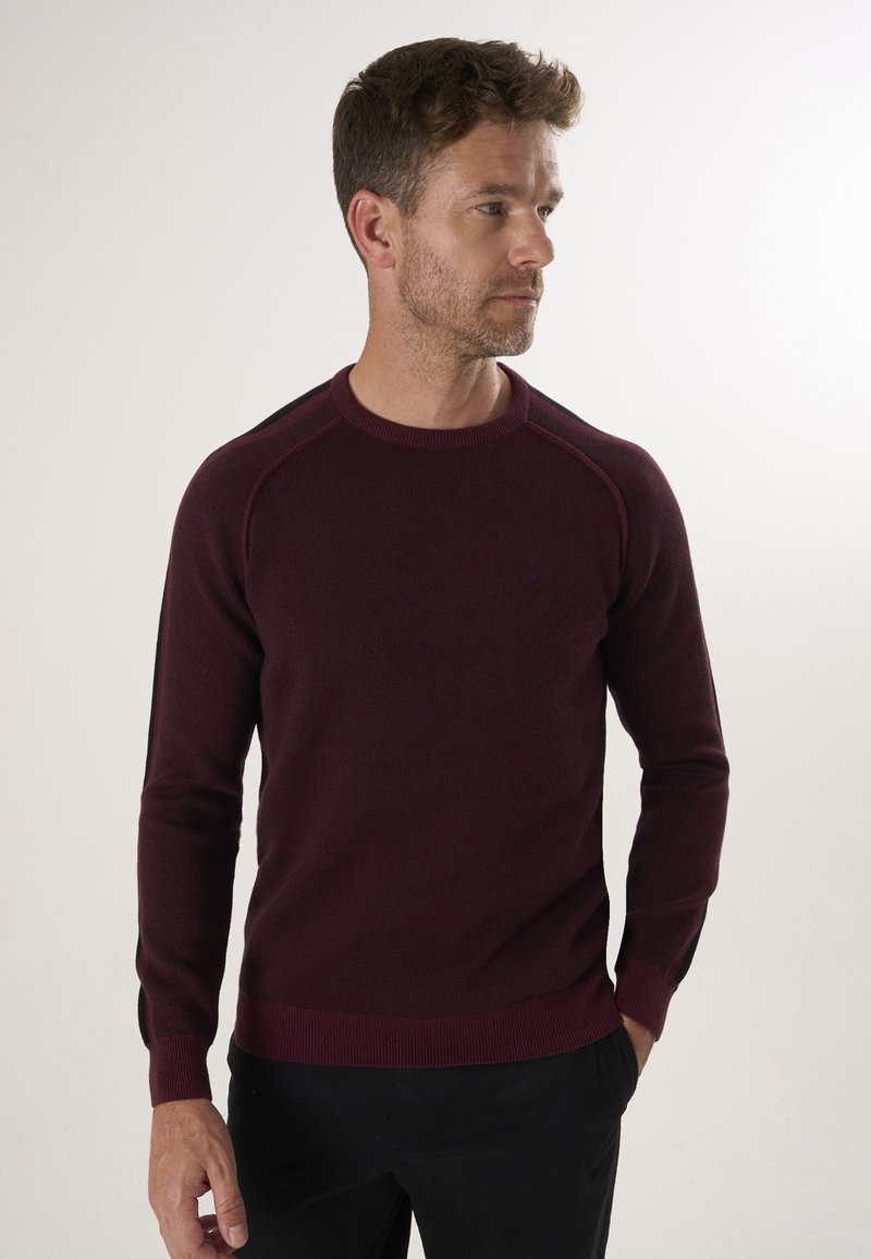 Bordeauxfarbener Pullover mit Rundhalsausschnitt, gerippten Bündchen und Saum. Mit kontrastierenden schwarzen Akzenten an den Schultern. Glatte Stricktexture.
