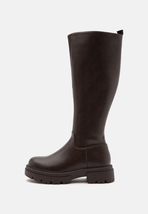 Bota alta de cuero marrón oscuro con suela gruesa y lengüeta trasera, mostrada de lado sobre un fondo blanco.