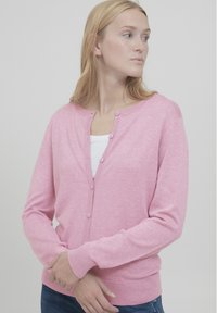 Vaaleanpunainen neuletakki, joka on valmistettu pehmeästä materiaalista, ja jossa on pyöreä kaula-aukko, pitkät hihat ja nappisulkemiset edessä.
