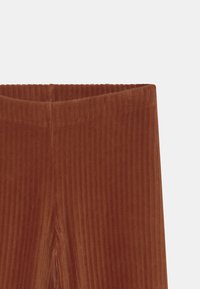 Geribde bruine corduroy broek met een zachte, gestructureerde stof en een elastische tailleband, wat zorgt voor een snug fit en een verticale streepjespatroon.