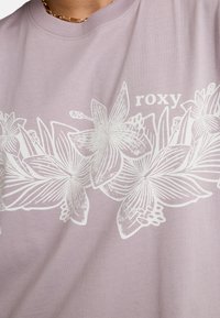 Lila t-shirt met een witte bloemenafbeelding en gedetailleerde bladvormen. Rond de halslijn en korte mouwen.