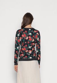 Svart tröja med lång ärm och blommönster med röda och vita rosor, accentuerad med en glittrande fåll och muddar. Mjukt, stretchigt material.