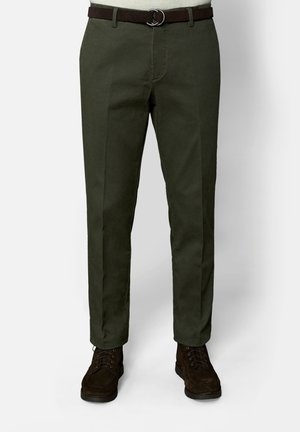 Donkergroene rechte broek gecombineerd met een donkerbruine riem en donkerbruine veterlaarzen, getoond van taille tot voeten.