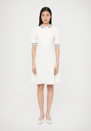 Weißes Polokleid mit kurzen Puffärmeln, braun gestreiftem Kragen und Bündchen sowie einem ausgestellten Schnitt. Das Material wirkt glatt und weich.