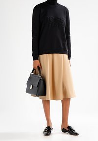 Černá mikina s reliéfním nápisem "BOSS ORANGE", béžová áčková sukně, černá strukturovaná kabelka a leskl�é černé slip-on boty.