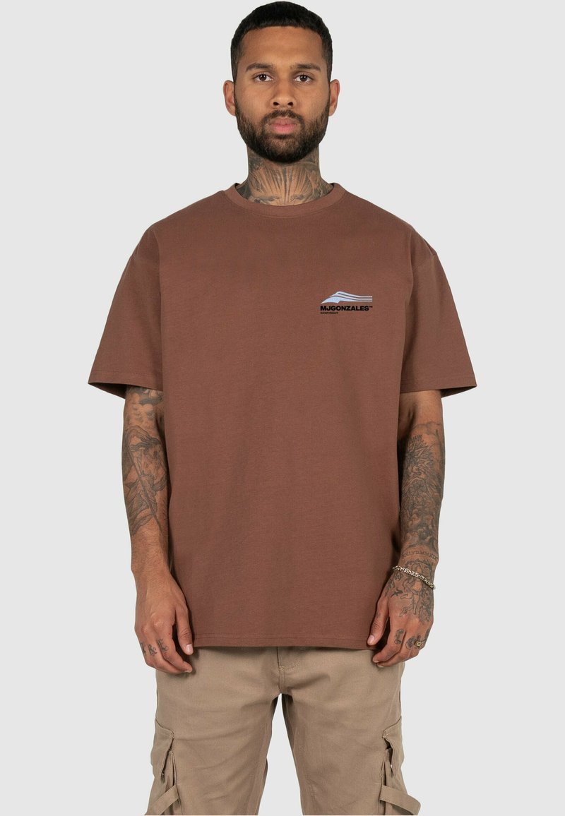 T-shirt en coton marron avec un col rond et des manches courtes, comportant un logo bleu et blanc sur la poitrine gauche. Design simple, coupe classique.