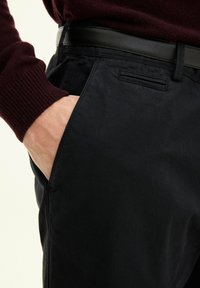 Zwarte katoenen broek met een slim fit, voorzien van een zijzak en een subtiele textuur. De tailleband heeft een stijlvolle zwarte riem.