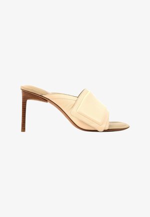 Mule beige con puntera abierta, una correa ancha acolchada y tacón de aguja de madera de altura media.