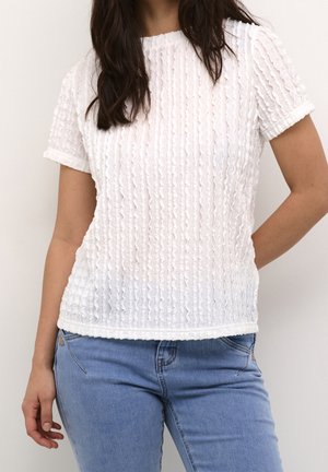 Witte top met korte mouwen en een gestructureerde, gerimpelde stof. Voorzien van een ronde halslijn en een zoom met een subtiele gerimpelde rand. Draagt een blauwe spijkerbroek.