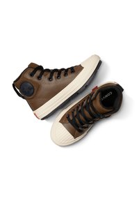 Bruine hoge sneakers van synthetisch leer, voorzien van zwarte veters, een rubberen neuskap en een ronde logopatch op de enkel.