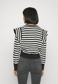 Felpa a righe bianche e nere con spalle arricciate e orlo a costine. Indossata con pantaloni attillati grigi scuri, vista da dietro.