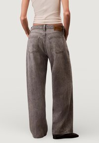 Harmaat kulahtaneet leveälahkeiset farkut, joissa on korkeavyötärö, takataskut ja merkitty nahkapatchi vyötäröllä.