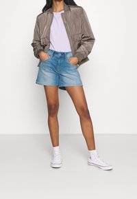 Lehká taupe bombera, levandulové tričko, modré džínové šortky a bílé vysoké tenisky. Ležérní outfit s kapsami.