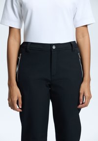 Sorte tætsiddende bukser med et elegant design, der har sidelommer med lynlås, en glat tekstur og en sølvfarvet knaplukning i taljen.
