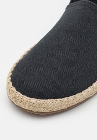 Svarte kanvas espadriller med såle i flettet juteseil, med en teksturert overdel og rund tå. Enkel design uten synlige dekorasjoner.