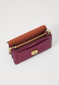Compact wallet in deep magenta leather with a smooth texture, featuring a gold-toned zipper and a brown suede flap on top.