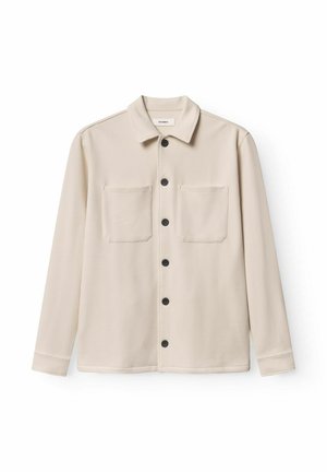 Woven beige shirt jacket with a textured finish, black buttons, two front pockets, and a pointed collar. Long sleeves and a straight hem.