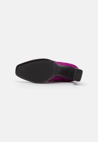 Zapato de ante fucsia con una suela de goma negra curvada. La suela presenta un patrón de agarre texturizado y un pequeño logo en el talón.