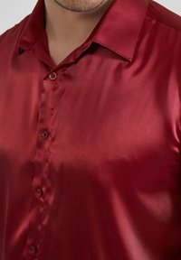 Chemise rouge en satin à manches courtes avec un col classique et une fermeture à boutons, dotée d'une texture lisse et brillante et d'un éclat subtil.