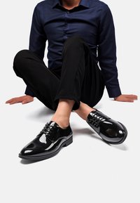 Scarpe eleganti in vernice nera con punta arrotondata, design con lacci e finitura liscia e lucida. Suola in gomma con leggero rialzo del tacco.