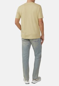 Lichtgele katoenen t-shirt met korte mouwen, ronde hals en een ontspannen fit, gecombineerd met lichtblauwe denim jeans en witte sneakers.