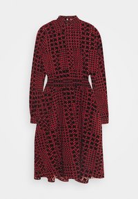 Röd och svart tryckt klänning med hög halsringning, långa ärmar och elastiskt midjeband. Har ett zigzag-mönster i kontrasterande färger.