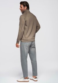 Sudadera beige para hombre con cuello alto, combinada con jeans de mezclilla gris claro y zapatillas blancas. Tejido suave con un diseño sencillo.
