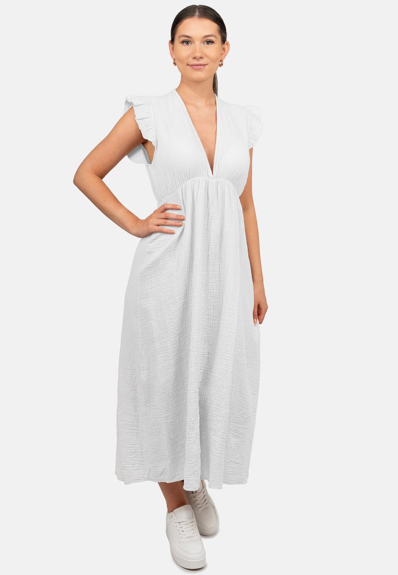 Robe blanche midi avec un décolleté en V profond, des manches courtes volantes et un tissu texturé ; portée avec des baskets blanches.