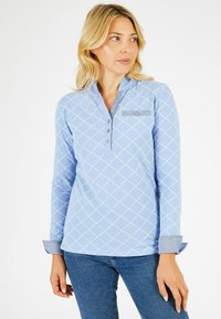 Chemise à manches longues bleu clair avec un motif de diamants et de points, patte de boutonnage à cinq boutons et accents en denim sur les poignets et la poche poitrine.