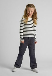 Randig långärmad ribbad topp i vit och svart, tillsammans med löst sittande kolderbyxor i kolgrått och vita sneakers.