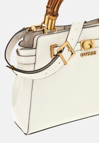 Biała torebka o fakturowanej powierzchni, z przestrzennym wzornictwem, złotymi elementami metalowymi i uchwytem przypominającym bambus. Posiada regulowany pasek i akcent z logo.