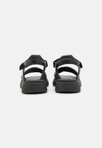 Zwarte sandalen met een platte zool, voorzien van verstelbare banden en een gladde leren afwerking. Minimalistisch ontwerp met branding op de hak.