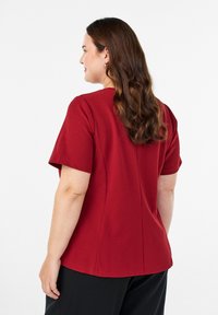 Czerwona bluzka z krótkim rękawem i okrągłym dekoltem, gładka w dotyku, doskonale dopasowana. Posiada subtelny detal szwu z tyłu, który dodaje charakteru.