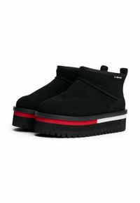 Botas de tobillo de ante negro con una suela gruesa negra, que cuentan con un acento a rayas rojas y blancas alrededor de la base y un diseño sin cordones.